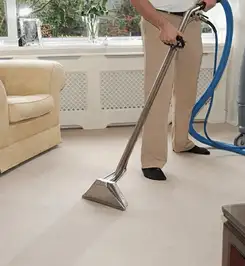 Professional carpet cleaner using a hot-water extraction wand and hose machine in a living room in Colorado Springs, CO.