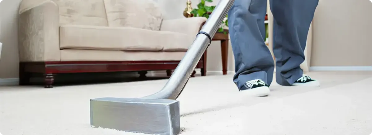Carpet cleaning technician using a hot-water extraction wand on a light-colored carpet in a living room, Colorado Springs, CO.