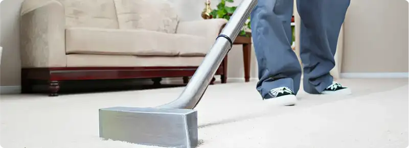 Carpet cleaning technician using a hot-water extraction wand on a light-colored carpet in a living room, Colorado Springs, CO.