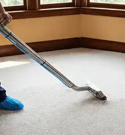 Steam carpet cleaning technician using a hot-water extraction wand on a residential carpet, wearing blue protective shoe covers Colorado Springs, CO.