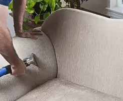 Professional upholstery cleaner deep-cleaning a fabric sofa with a handheld extraction tool and hose in Colorado Springs, CO.